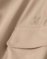 Close-up of the MENS LLOYD CARGO JOGGER - B6P159B200 by Psycho Bunny, featuring a beige fabric adorned with a snap fastening pocket. Above the pocket is a stitched bunny logo with crossed bones underneath its head, showcasing a subtle pirate motif. The playful embroidery refinement adds an elegant touch to the smooth and well-crafted fabric.