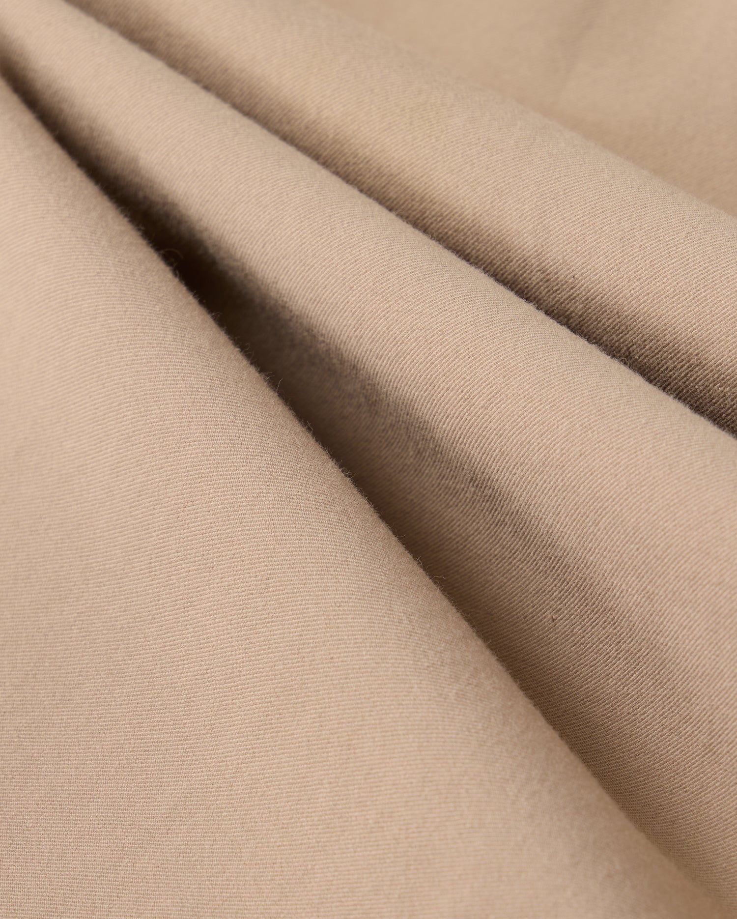 Close-up of beige fabric with a soft, smooth texture and subtle folds. The material appears lightweight and finely woven, suggesting it could be used for clothing or upholstery. The color and texture give a cozy and comfortable impression, making it perfect for the Psycho Bunny MENS LLOYD CARGO JOGGER - B6P159B200's snap fastening pockets.