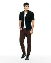 Black ribbed knit short-sleeve collared shirt with embroidered Psycho Bunny skull logo on chest, layered over a white tee, paired with slim-fit brown Mens Maverick 10k Step Pant.