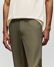 A person wears Psycho Bunny MENS MAVERICK 10K STEP PANT - B6P788D200 in olive green, featuring five-pocket styling, paired with a cream shirt. The image focuses on the pants and midsection; the person’s face is not visible.