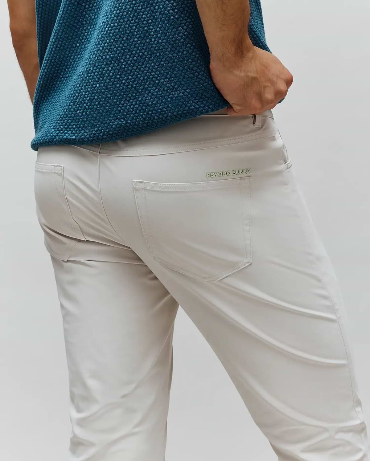 Mens Maverick 10k Step Pant, light beige slim-fit performance fabric with a small, embroidered green Psycho Bunny wordmark above the back right pocket.