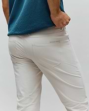 Mens Maverick 10k Step Pant, light beige slim-fit performance fabric with a small, embroidered green Psycho Bunny wordmark above the back right pocket.