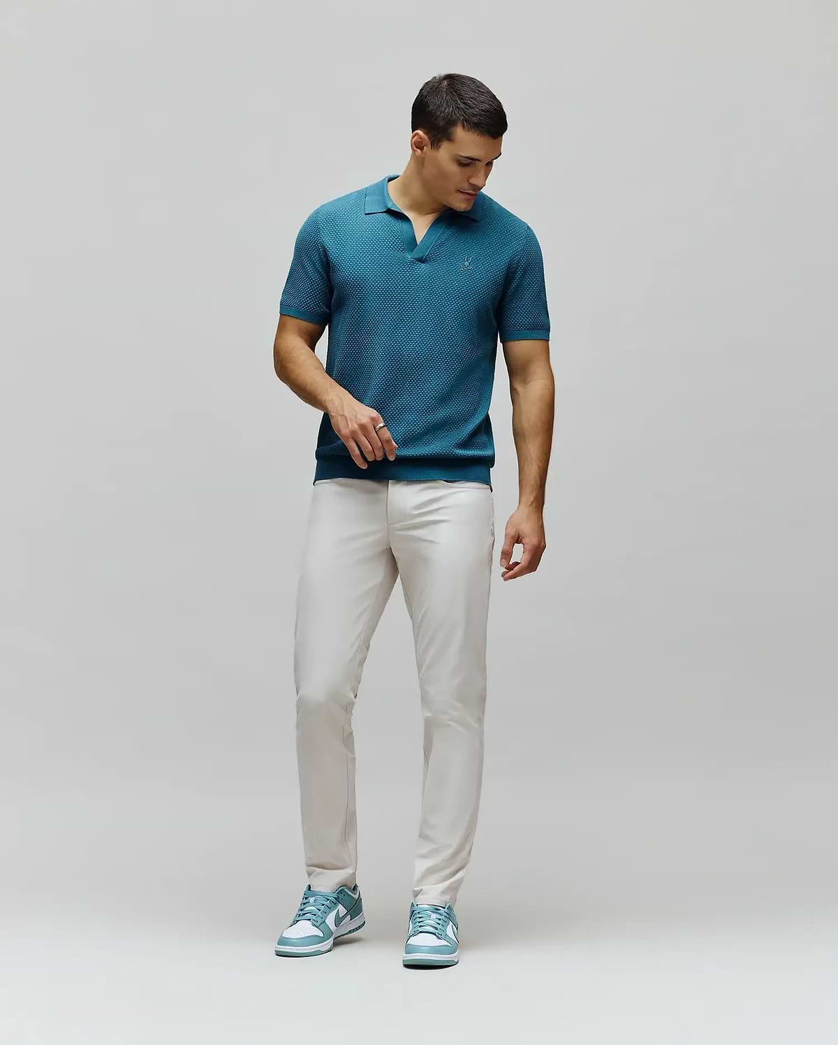 Teal textured knit polo with a tonal embroidered Psycho Bunny skull logo on the chest, paired with slim fit light beige Mens Maverick 10k Step Pant.