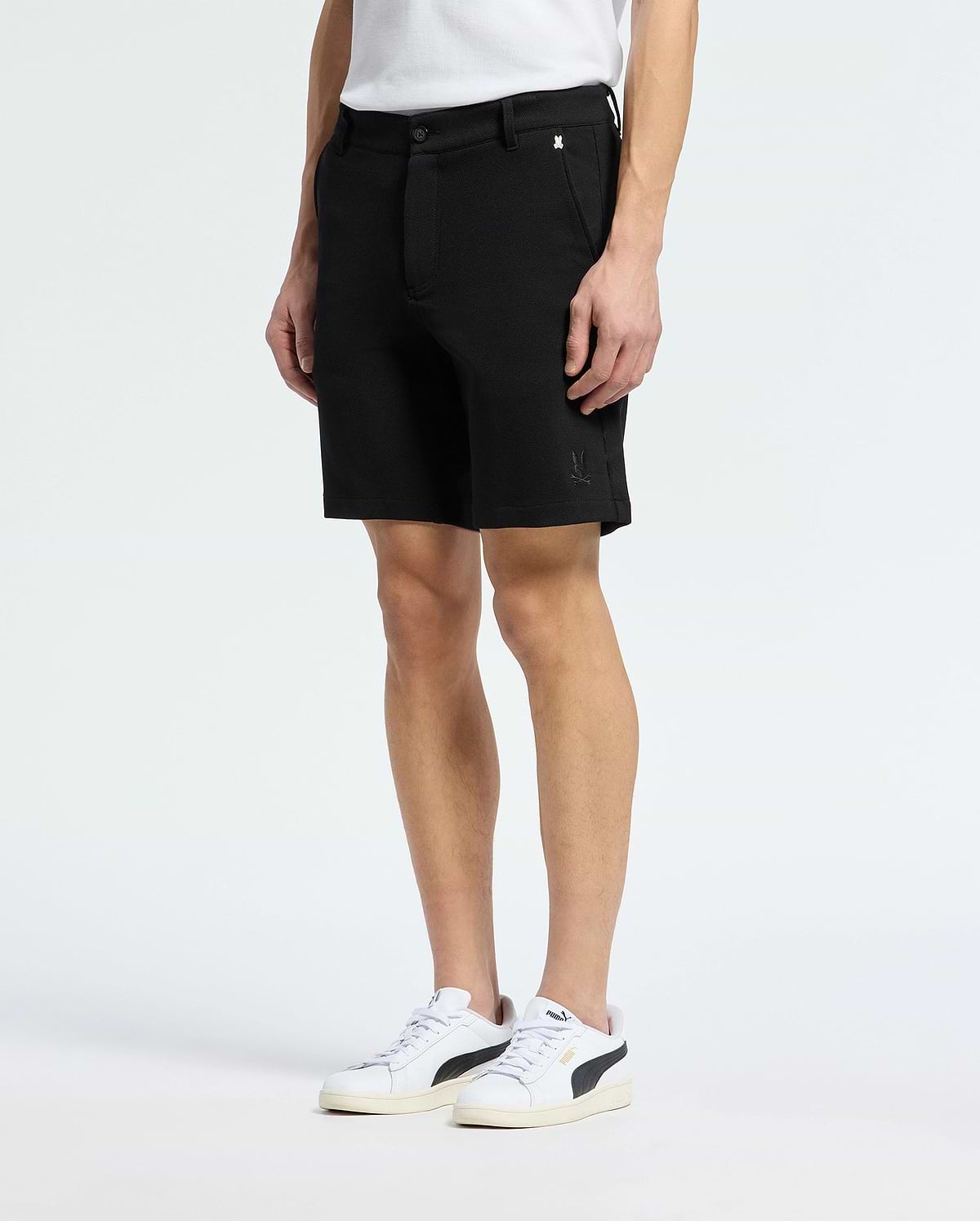 A person in MENS SHIRO KNIT HONEYCOMB SHORT by Psycho Bunny, paired with black and white sneakers, stands against a plain white background. The subtle logo near the hem adds flair to these versatile shorts.