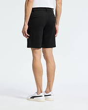 A person stands with their back to the camera, wearing a white shirt and the Psycho Bunny MENS SHIRO KNIT HONEYCOMB SHORT - B6R585F200. White sneakers with black accents complete the look against a plain background, showcasing a stylish transition for any setting.