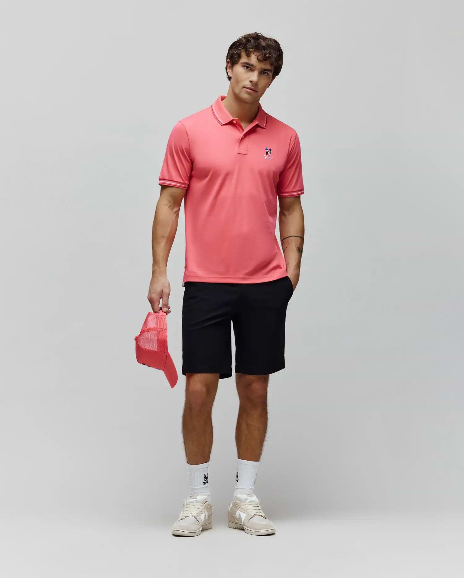 Coral pink pique polo with white tipped collar and cuffs, featuring a small embroidered blue and red Psycho Bunny skull logo on the left chest, paired with classic fit black Mens Maverick 10k Step Short.