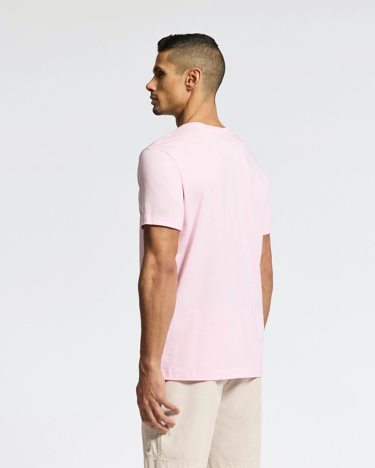 A man models a versatile light pink Psycho Bunny Classic Crew Neck Tee (B6U014CRPC) and beige shorts, standing slightly to the side against a plain white backdrop, accentuating the pima cotton fabric.