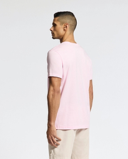 A man models a versatile light pink Psycho Bunny Classic Crew Neck Tee (B6U014CRPC) and beige shorts, standing slightly to the side against a plain white backdrop, accentuating the pima cotton fabric.