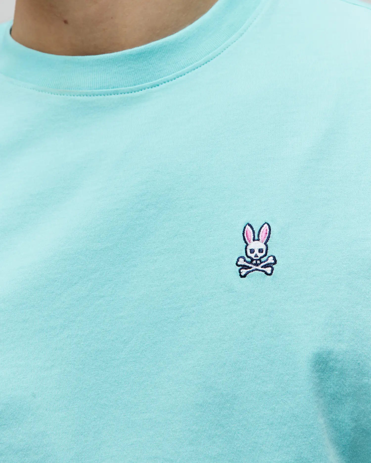 Mens Classic Crew Neck Tee in vibrant aqua jersey knit, showcasing the iconic small embroidered Psycho Bunny skull logo with pink ears, white skull, and black crossbones on the left chest, embodying refined streetwear.