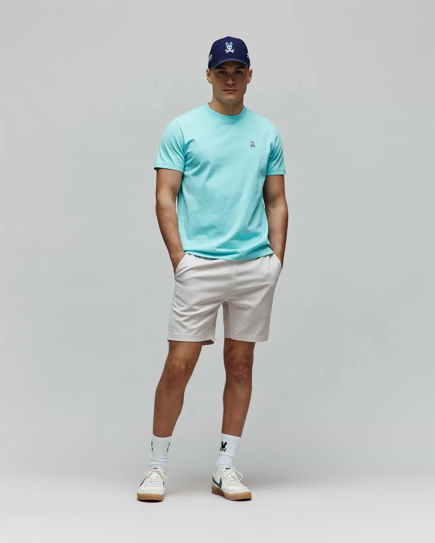Mens Classic Crew Neck Tee in aqua jersey with small embroidered Psycho Bunny logo, paired with light beige shorts, a navy cap with light blue embroidered logo, and white socks with a black bunny skull.