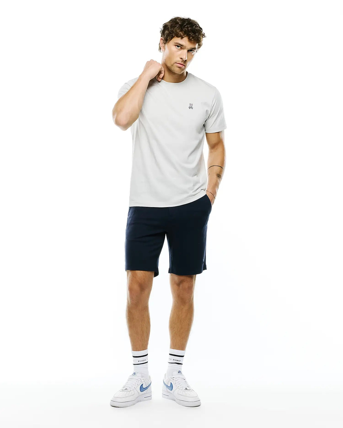 Mens Classic Crew Neck Tee in light grey jersey, featuring a small embroidered Psycho Bunny skull logo on the left chest, styled with navy blue classic fit shorts.
