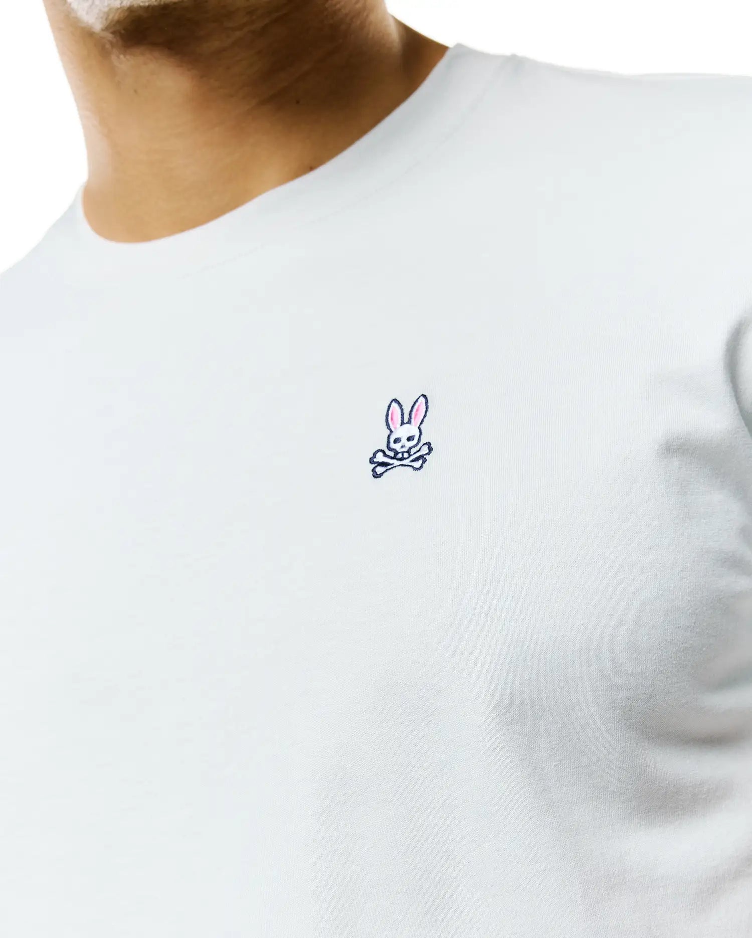 Mens Classic Crew Neck Tee in light blue jersey knit, featuring a classic fit and a small, embroidered Psycho Bunny skull logo with pink ears on the left chest.