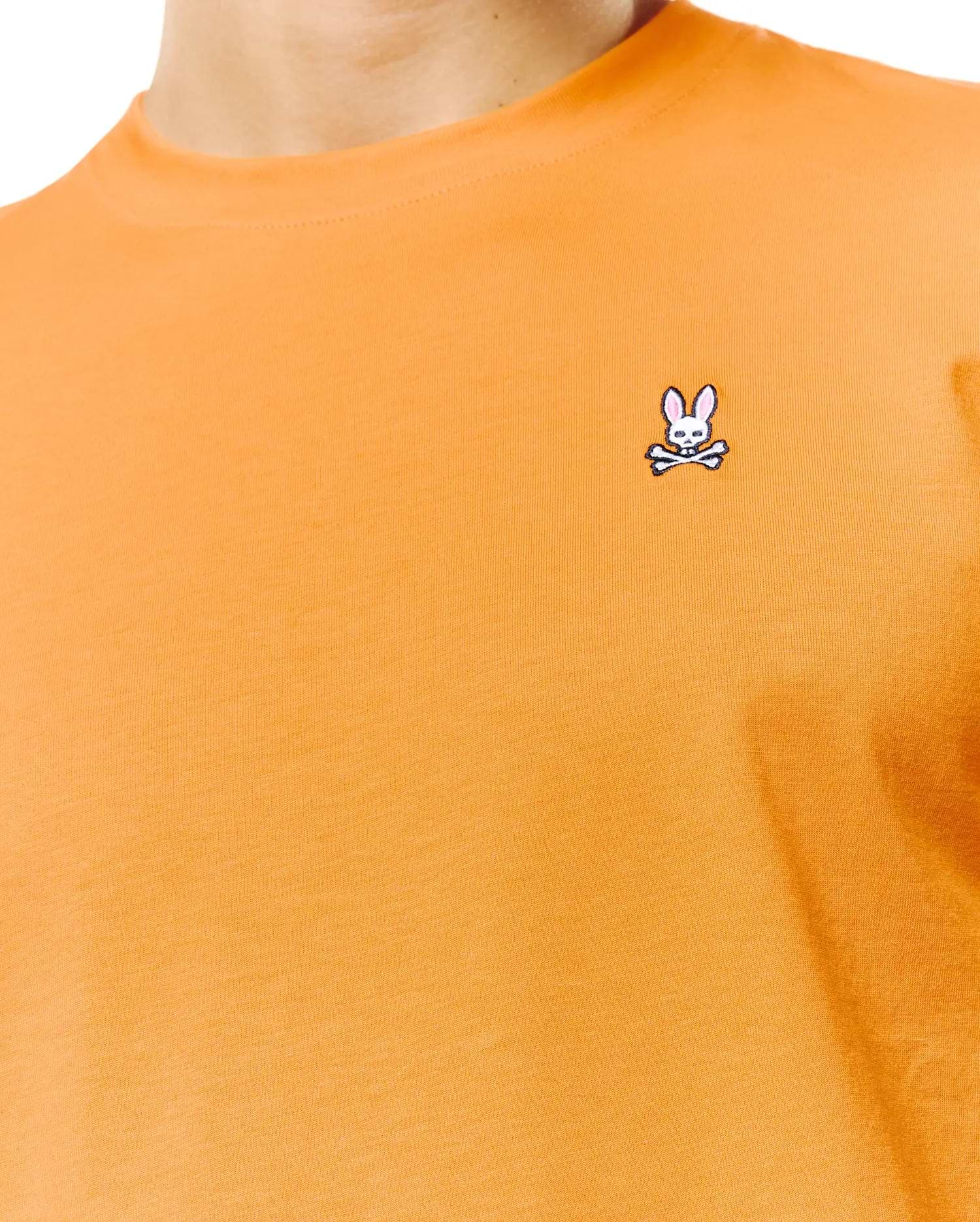 Mens Classic Crew Neck Tee in vibrant orange jersey knit, featuring a small embroidered white and pink Psycho Bunny skull logo on the left chest.
