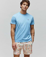 Mens Classic Crew Neck Tee in light blue jersey, with a small embroidered Psycho Bunny skull logo on the left chest. Paired with cream multi-color plaid shorts featuring repeating bunny skull patterns.