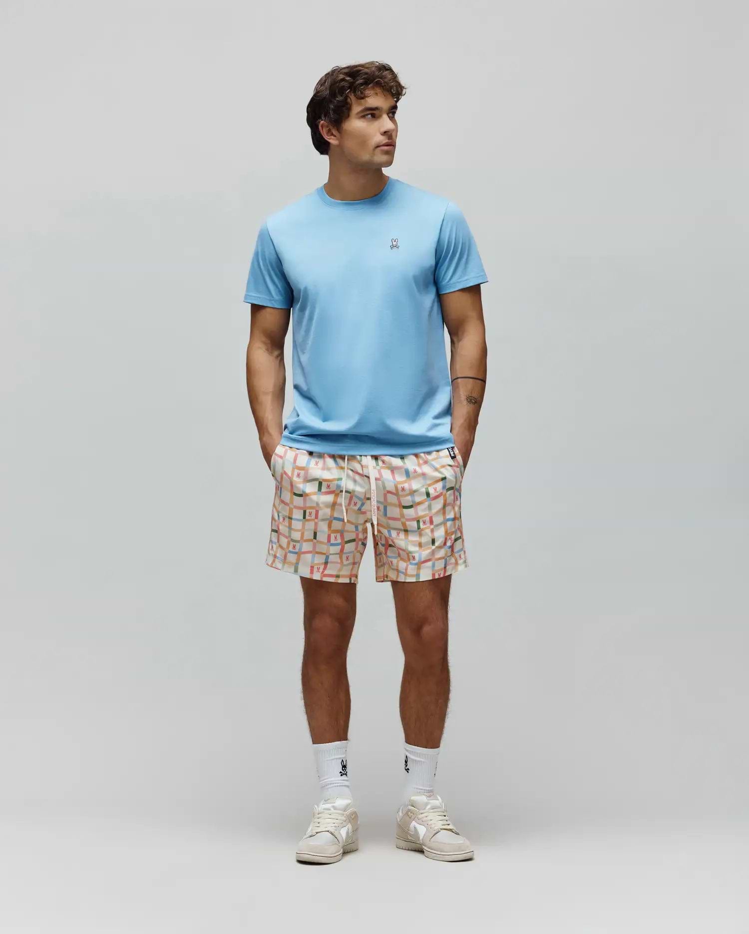 Light blue Mens Classic Crew Neck Tee, classic fit jersey, with small embroidered Psycho Bunny skull logo. Paired with cream relaxed fit shorts, vibrant multi-color grid pattern, and integrated bunny skull logos.