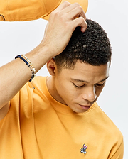 Mens Classic Crew Neck Tee in golden yellow, featuring a smooth jersey knit and a small, embroidered Psycho Bunny skull logo on the left chest with pink, grey, and white accents.