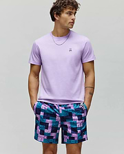 Mens Classic Crew Neck Tee, lavender jersey, with embroidered Psycho Bunny skull logo on left chest. Paired with relaxed shorts in a teal and purple pixelated patchwork pattern with repeated Psycho Bunny logos.