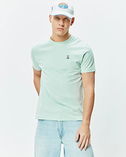Mens Classic Crew Neck Tee in a vibrant mint green, crafted from soft jersey fabric, featuring a small embroidered black, white, and pink Psycho Bunny skull logo on the left chest, offering a classic fit.