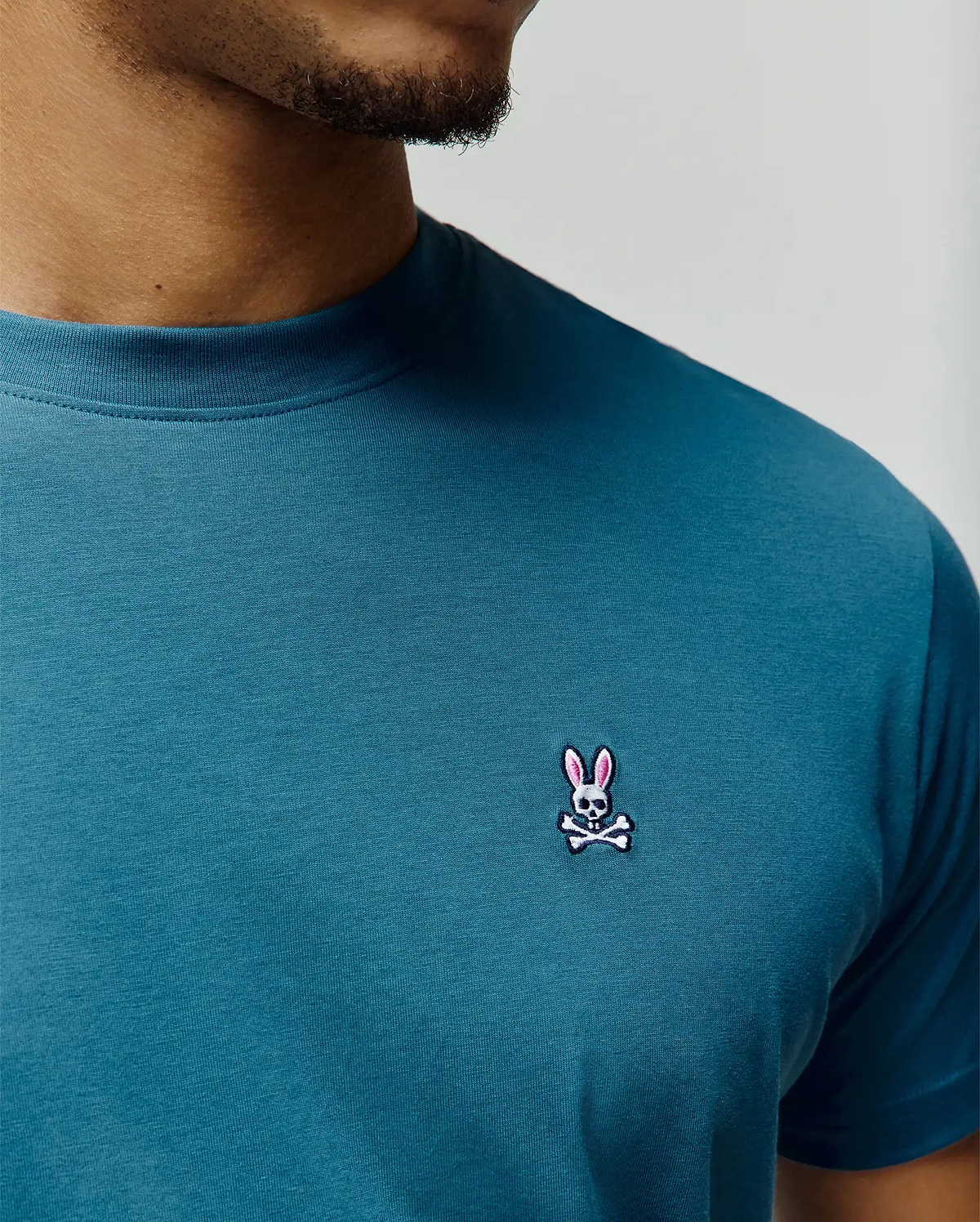 Mens Classic Crew Neck Tee in deep teal jersey knit, featuring a small, intricately embroidered Psycho Bunny skull logo with pink ears on the left chest, offering a classic fit.
