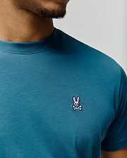 Mens Classic Crew Neck Tee in deep teal jersey knit, featuring a small, intricately embroidered Psycho Bunny skull logo with pink ears on the left chest, offering a classic fit.