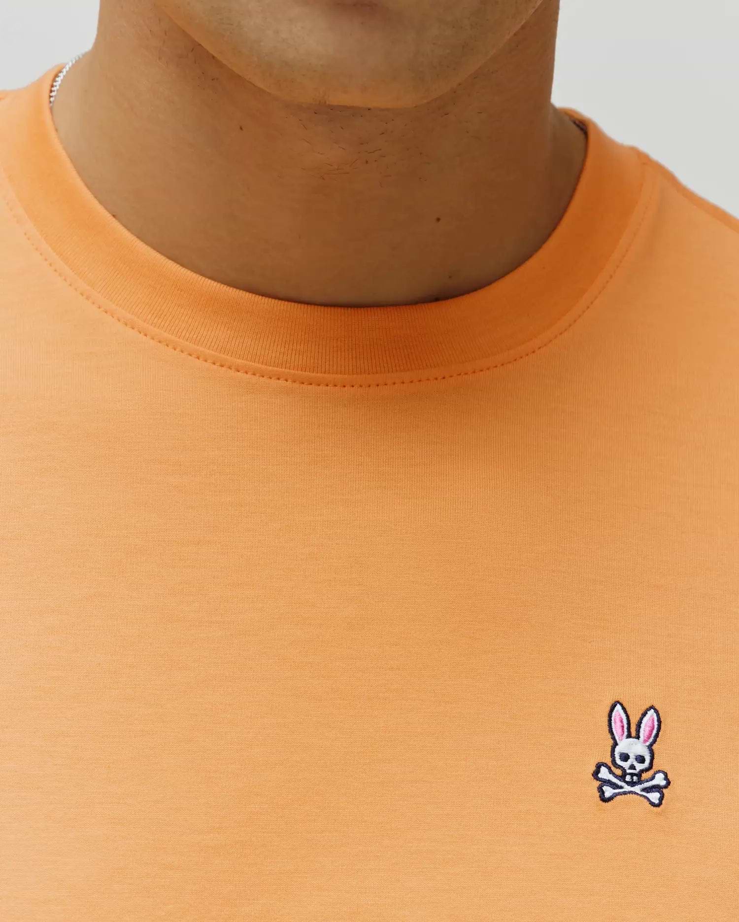 Mens Classic Crew Neck Tee in peach, featuring a classic fit and smooth jersey knit. Small embroidered Psycho Bunny skull logo with pink ears, white skull, and black outline on the left chest.