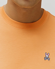 Mens Classic Crew Neck Tee in peach, featuring a classic fit and smooth jersey knit. Small embroidered Psycho Bunny skull logo with pink ears, white skull, and black outline on the left chest.