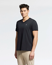 A person faces the camera wearing a black Psycho Bunny MENS CLASSIC V NECK TEE - B6U100ARPC in Pima cotton with a small white embroidered logo on the chest and beige pants, set against a plain white background.