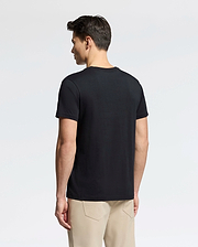 A person with short dark hair, standing sideways against a light gray background, wears a black MENS CLASSIC V NECK TEE - B6U100ARPC by Psycho Bunny and beige pants.