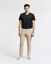 Against a white backdrop, a man models effortless style wearing Psycho Bunny's MENS CLASSIC V NECK TEE (B6U100ARPC) in black. He pairs it with beige pants, white sneakers with black details, and a wristwatch. With short dark hair and relaxed posture, he exudes laid-back elegance.