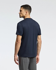 A man stands with his back to the camera, wearing a Psycho Bunny MENS CLASSIC V NECK TEE - B6U100ARPC in navy and gray pants. The background is a simple, light gray.