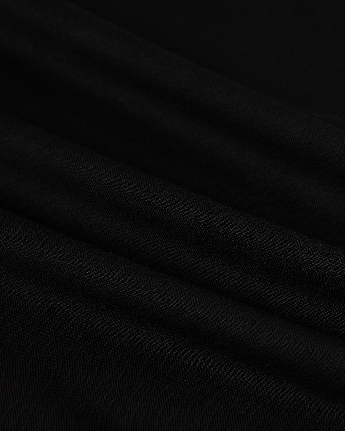 Close-up of the MENS HAWAII CITY TEE - B6U169Y1PC by Psycho Bunny, made from black Pima cotton fabric with a smooth, slightly rippled texture. The dark material displays gentle folds and a subtle sheen, resembling the luxurious quality of a sophisticated men's T-shirt for an elegant appearance.