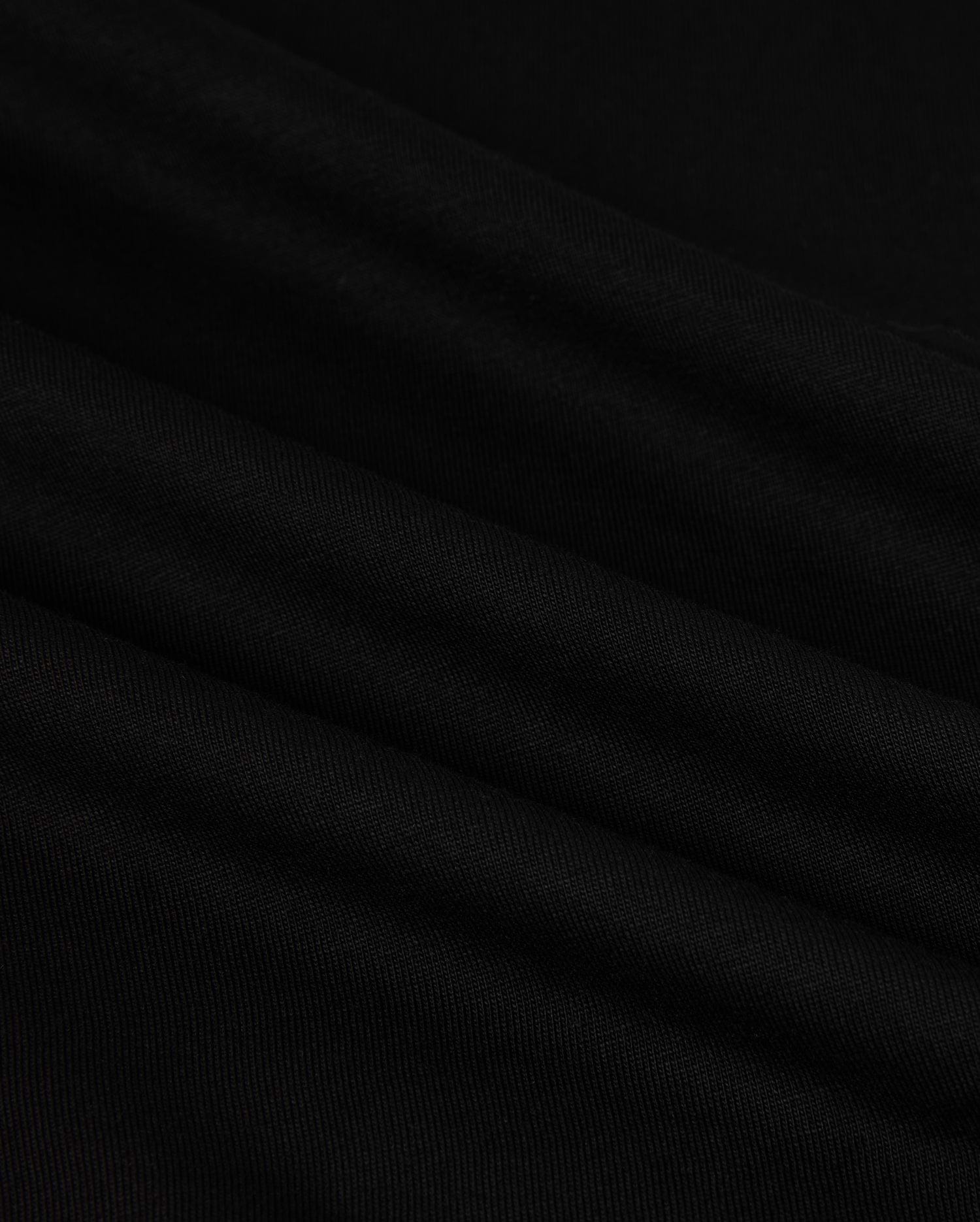 Close-up of the MENS HAWAII CITY TEE - B6U169Y1PC by Psycho Bunny, made from black Pima cotton fabric with a smooth, slightly rippled texture. The dark material displays gentle folds and a subtle sheen, resembling the luxurious quality of a sophisticated men's T-shirt for an elegant appearance.