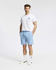 A man stands against a plain background, wearing the Psycho Bunny MENS MONTREAL TEE (B6U381F200), paired with light blue drawstring shorts, white crew socks, and white sneakers. His hands are in his pockets and he faces the camera.