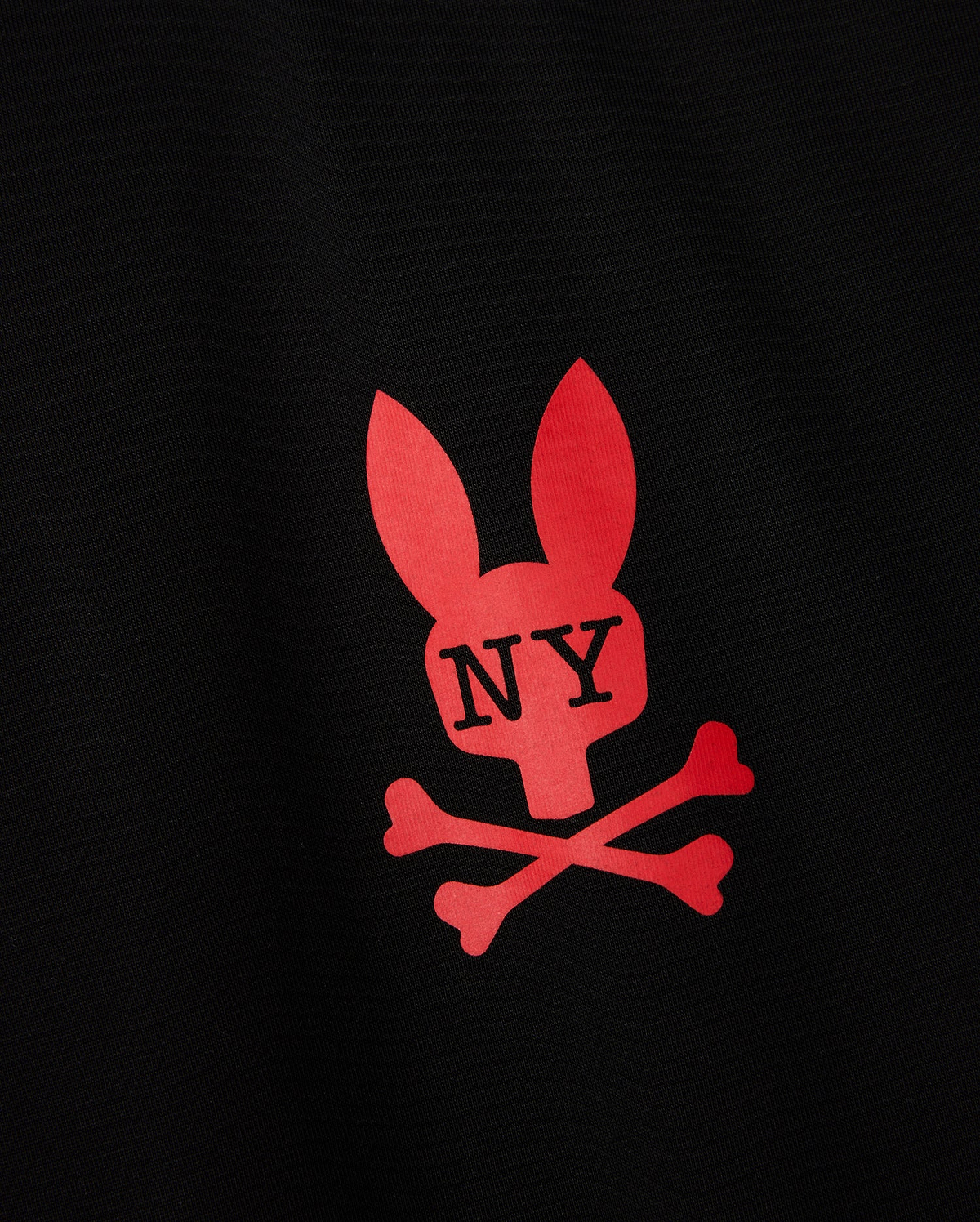 The **MENS NEW YORK TEE - B6U554W1PC** by **Psycho Bunny** showcases a black background with a striking red graphic of a stylized bunny head featuring long ears and a skull-like face. The letters "NY" are in black, centrally located on the head. Below this, two red bone shapes intersect to form an "X." This distinctive New York tee is crafted from ultra-soft Pima cotton for ultimate comfort.