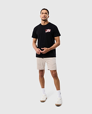 A man wearing a black Psycho Bunny ATLANTA CITY Tee with a red logo, beige shorts, and white sneakers standing against a plain white background.