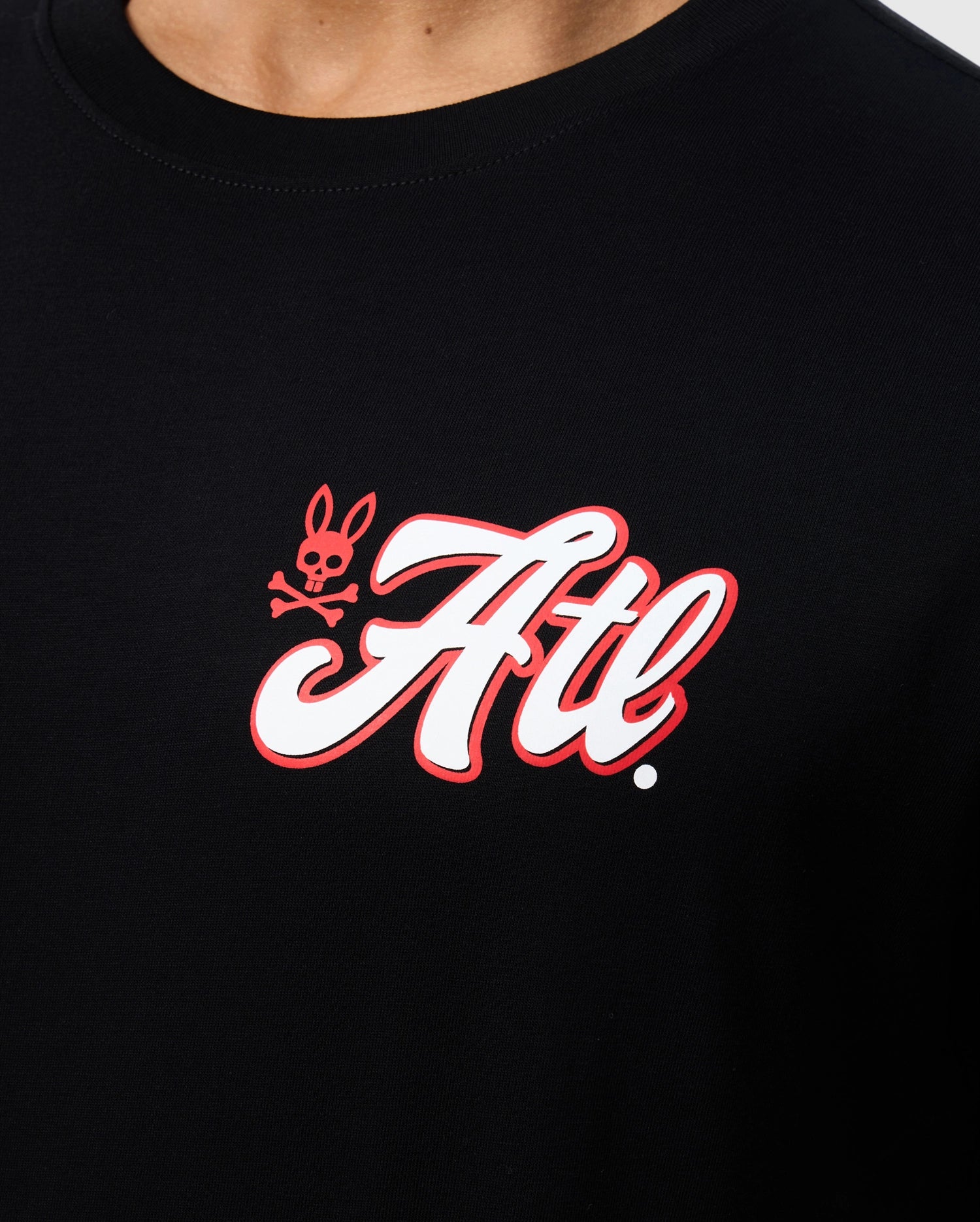 Close-up of a black Psycho Bunny Atlanta Tee with a red and white logo that reads "ATL" in cursive script, accompanied by a small, stylized rabbit icon on the left side.