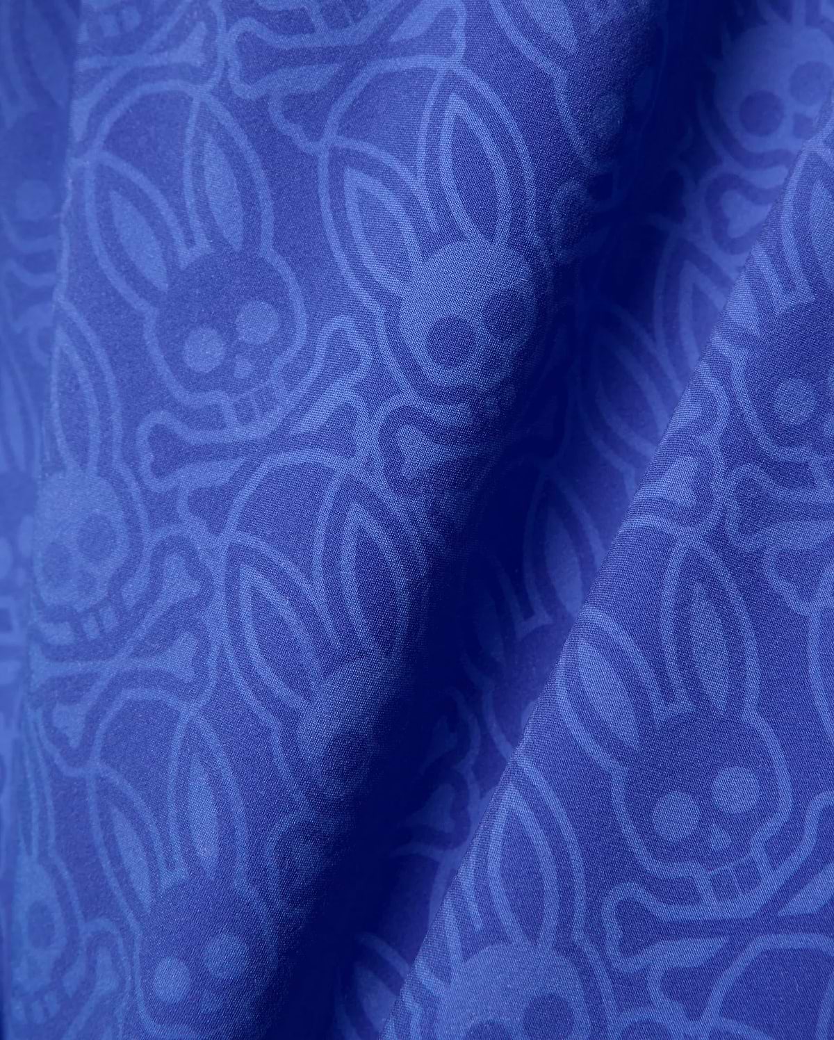 Mens Samos Hydrochromic Printed Swim Trunk in royal blue, featuring a subtle tonal all-over Psycho Bunny skull and crossbones logo pattern on smooth fabric.