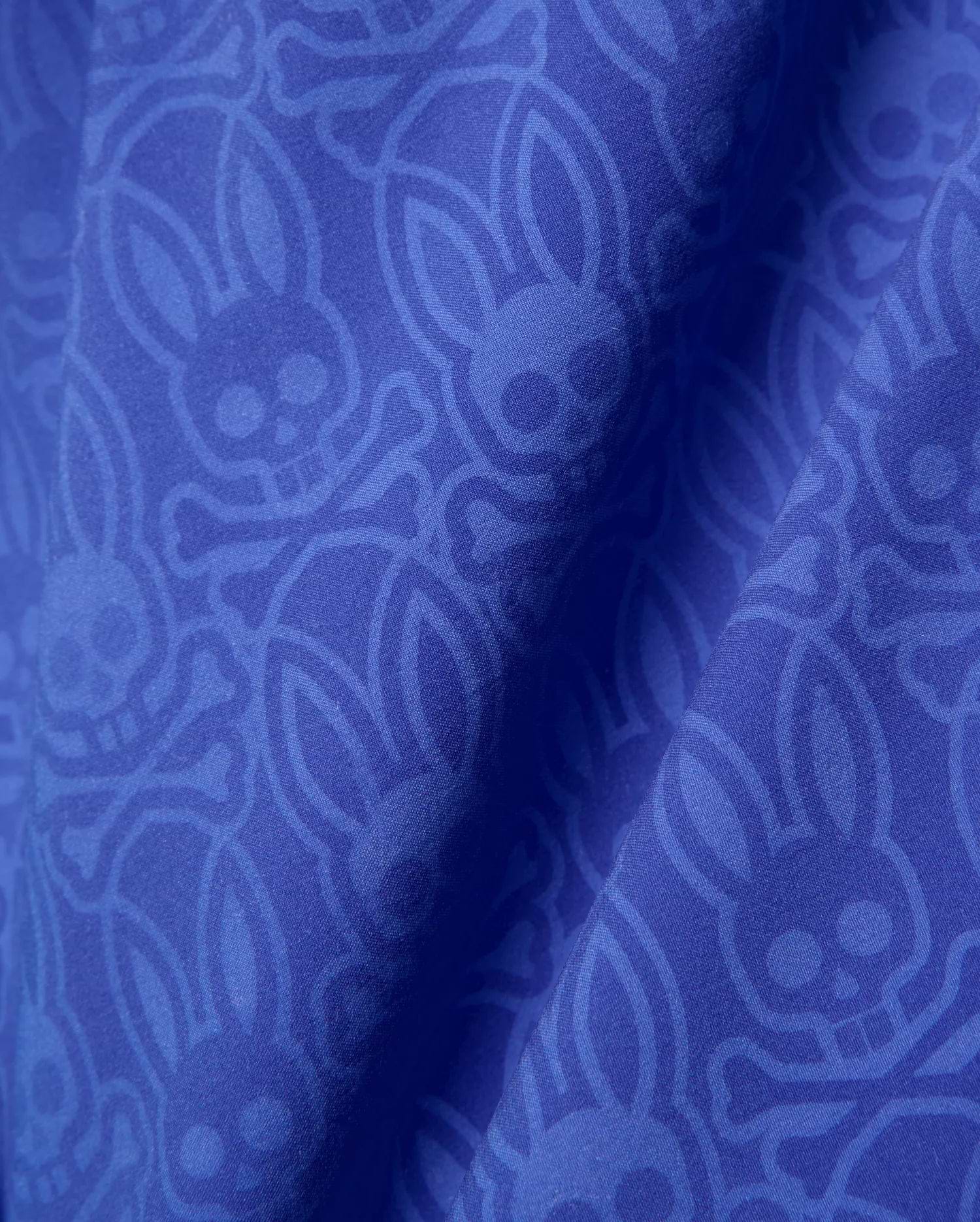 Mens Samos Hydrochromic Printed Swim Trunk in royal blue, featuring a subtle tonal all-over Psycho Bunny skull and crossbones logo pattern on smooth fabric.