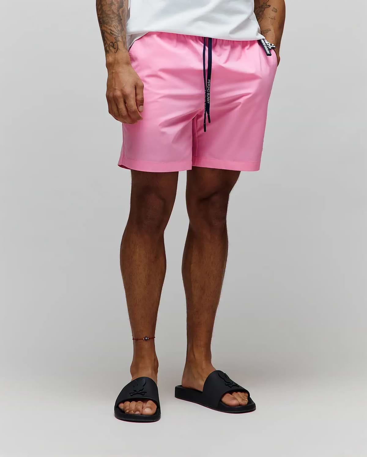 Mens Samos Hydrochromic Printed Swim Trunk in pink, featuring a relaxed fit, smooth quick-dry fabric, navy drawstring with white Psycho Bunny branding, and a small black bunny skull logo tag on the right hip.