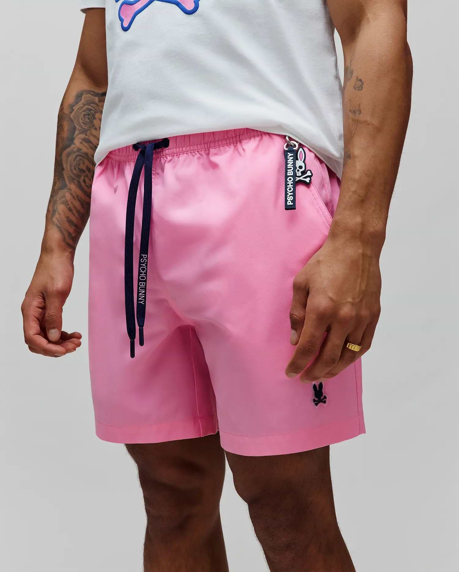 Mens Samos Hydrochromic Printed Swim Trunk, pink with a relaxed fit, smooth fabric, navy Psycho Bunny drawstrings, embroidered black bunny skull logo on left leg, and a Psycho Bunny keychain.