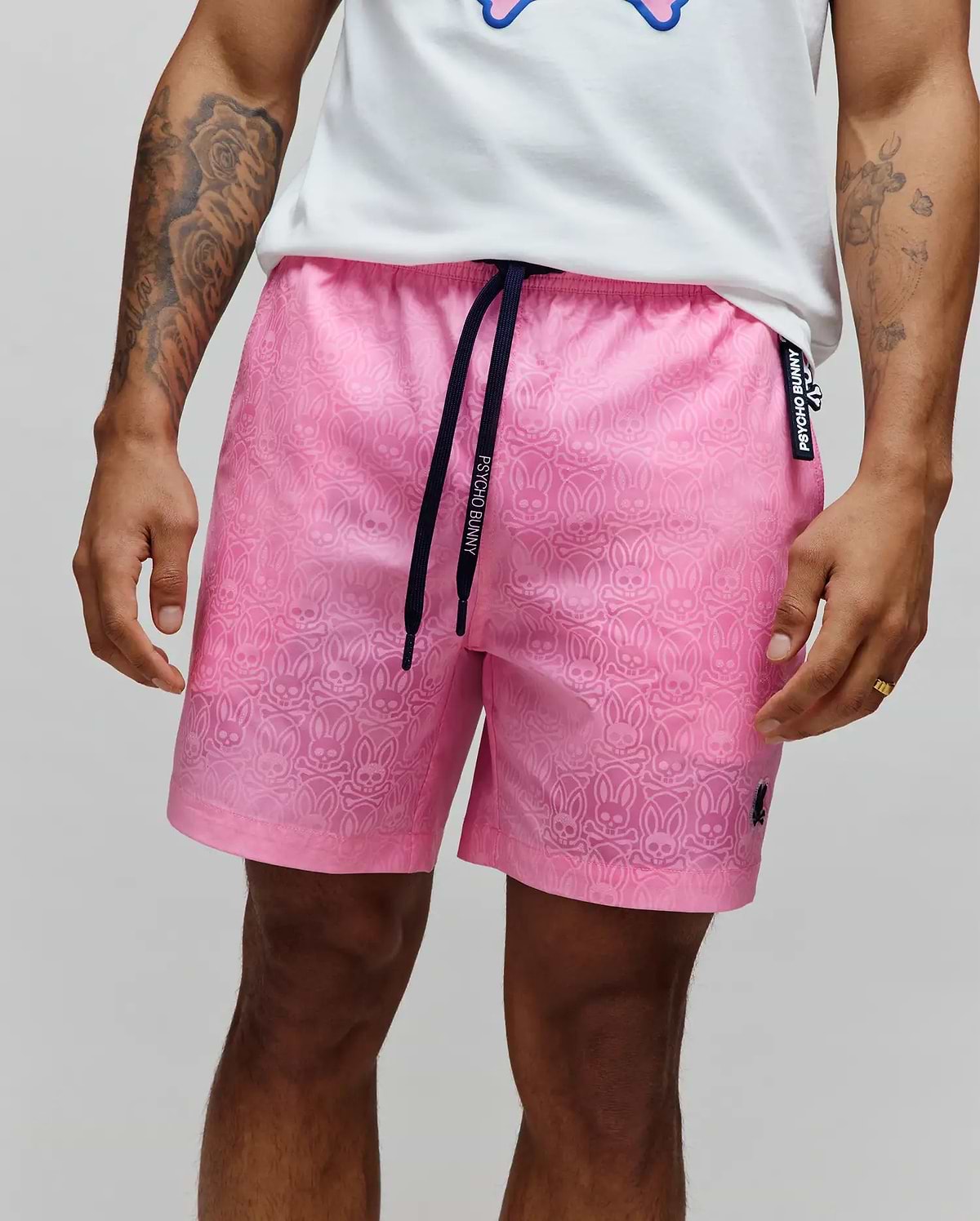 Mens Samos Hydrochromic Printed Swim Trunk, pink, with all-over hydrochromic bunny skull print, dark navy Psycho Bunny branded drawstring, small black embroidered bunny logo on left leg, and Psycho Bunny side tag.