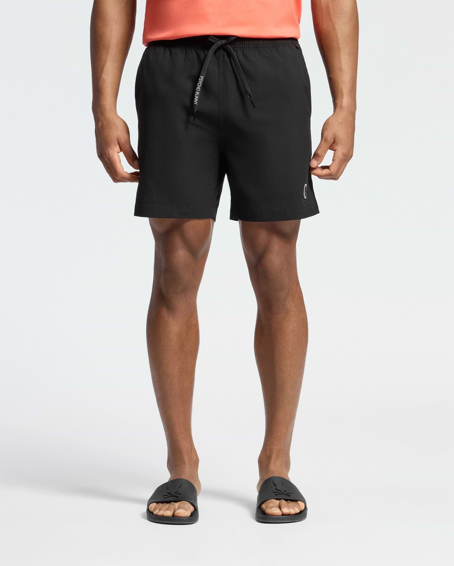 Black Mens Samos Hydrochromic Printed Swim Trunk with a classic fit, featuring a smooth fabric, white PSYCHO BUNNY text on the drawstring, and a small silver bunny skull logo on the lower left leg.
