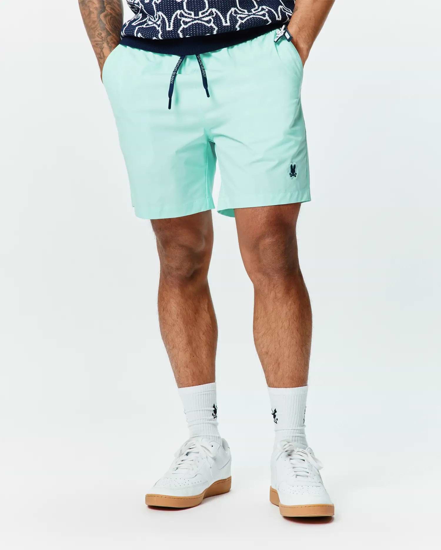 Mens Samos Hydrochromic Printed Swim Trunk 6, light mint green with a classic fit, smooth quick-dry fabric, navy drawstring featuring Psycho Bunny text, and a small embroidered navy bunny skull logo on the left leg.