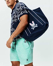 Navy textured knit polo with white abstract bunny pattern, Mens Samos Hydrochromic Printed Swim Trunk 6 in mint green with tonal bunny skull print and small embroidered logo, plus a navy tote with large pink-eared bunny skull logo.
