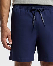 A person in Psycho Bunny MENS SAMOS Hydrochromic printed swim trunks (navy blue) with branded drawstrings and a gray shirt; only their lower torso and upper legs are shown.