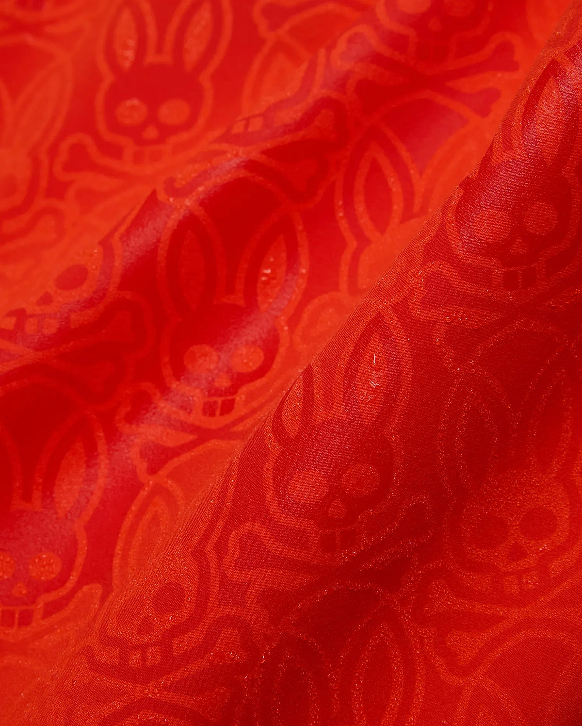 Mens Samos Hydrochromic Printed Swim Trunk in vibrant red, featuring a subtle tonal allover Psycho Bunny skull and crossbones pattern on smooth, slightly textured fabric.