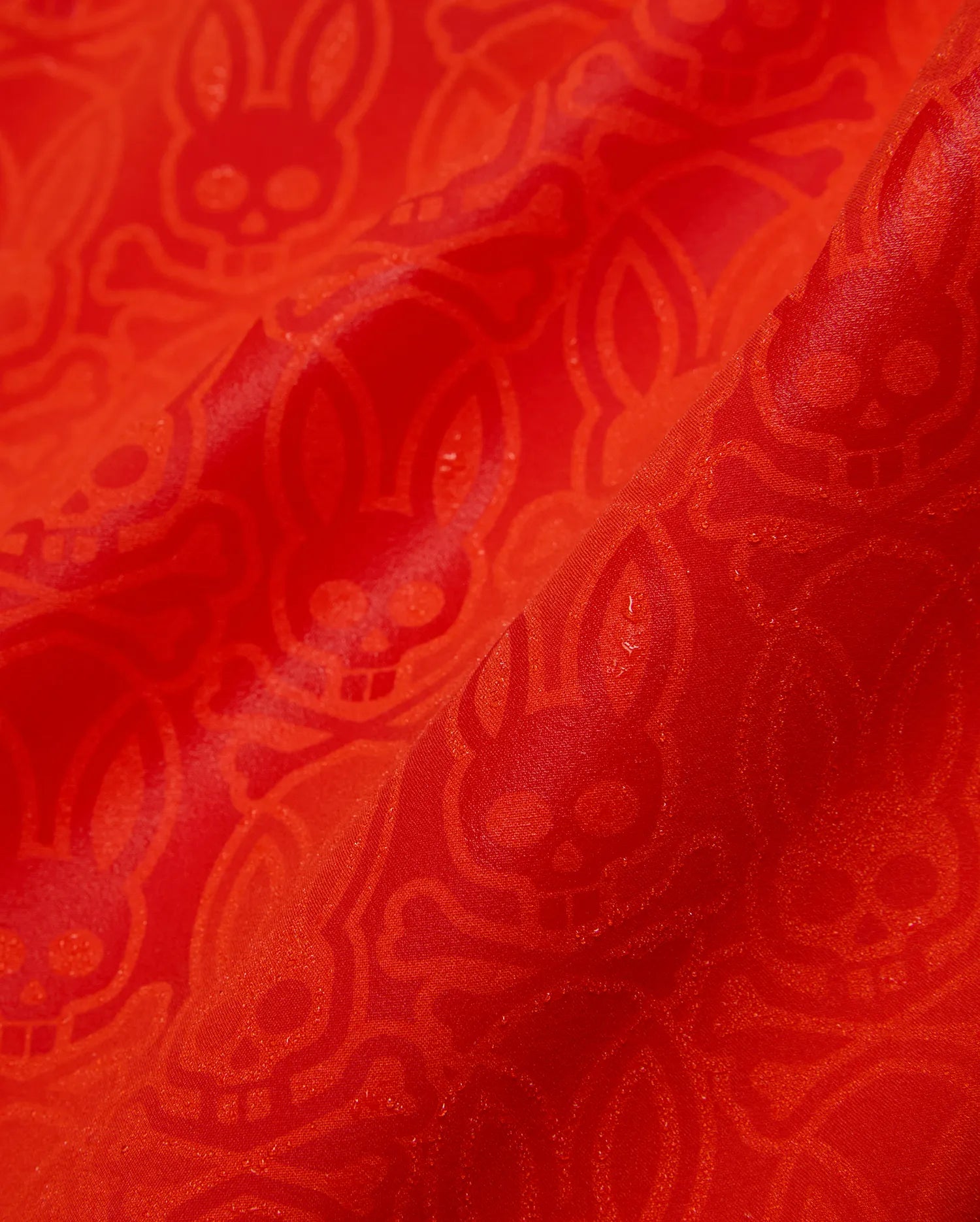 Mens Samos Hydrochromic Printed Swim Trunk in vibrant red, featuring a subtle tonal allover Psycho Bunny skull and crossbones pattern on smooth, slightly textured fabric.