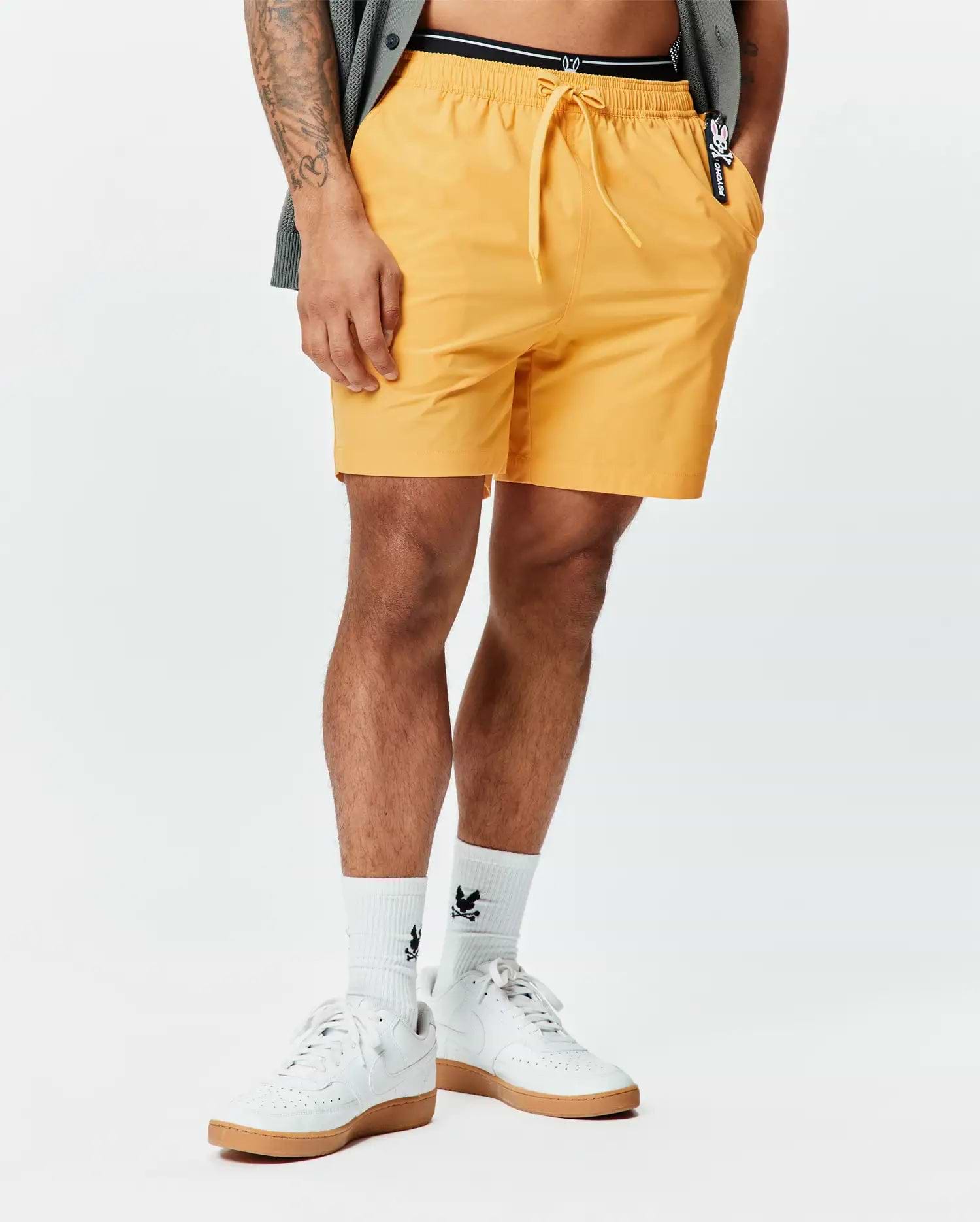Mens Samos Hydrochromic Printed Swim Trunk in vibrant yellow, featuring a relaxed fit, drawstring waist, smooth quick-dry fabric, and a small black and white Psycho Bunny logo tag on the right pocket. (2)