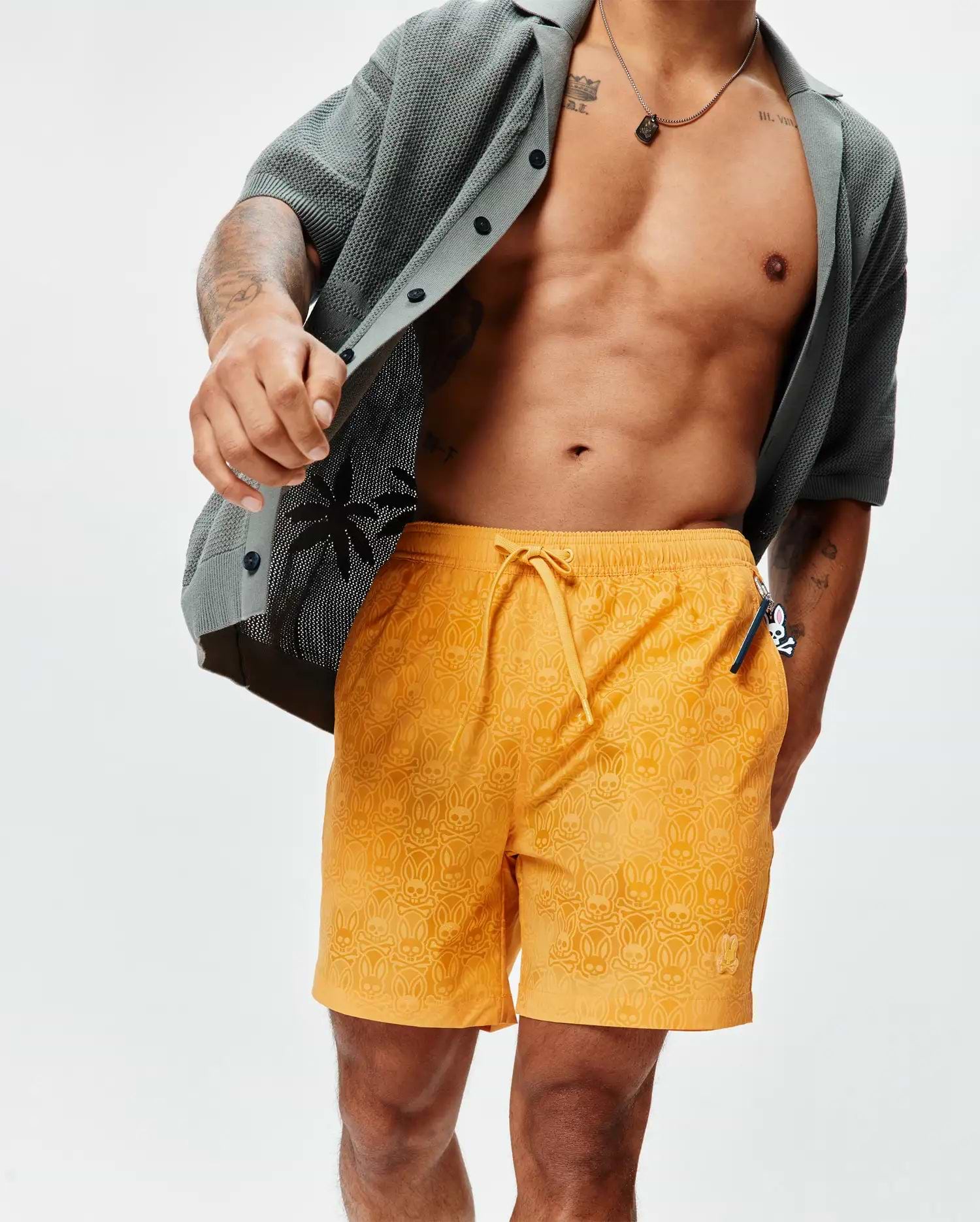 Mens Samos Hydrochromic Printed Swim Trunk in vibrant orange, featuring an all-over subtle hydrochromic Psycho Bunny skull and crossbones print, drawstring waist, and small embroidered bunny logo on the left leg, offering a relaxed fit. (3)