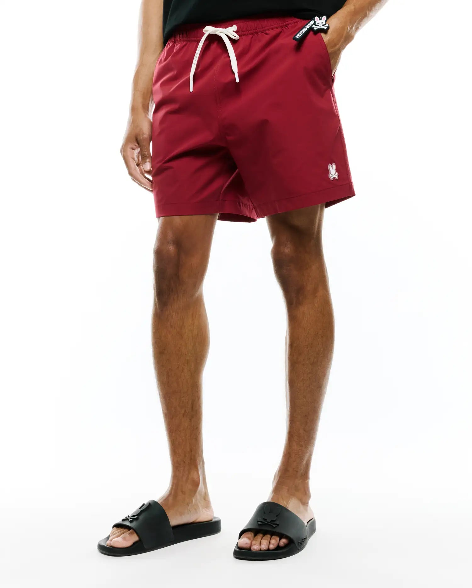 Samos Hydrochromic Printed Swim Trunk in deep red, featuring a relaxed fit, smooth quick-dry fabric, white drawstring, small embroidered white Psycho Bunny skull logo on the left leg, and a black Psycho Bunny tag on the right pocket.